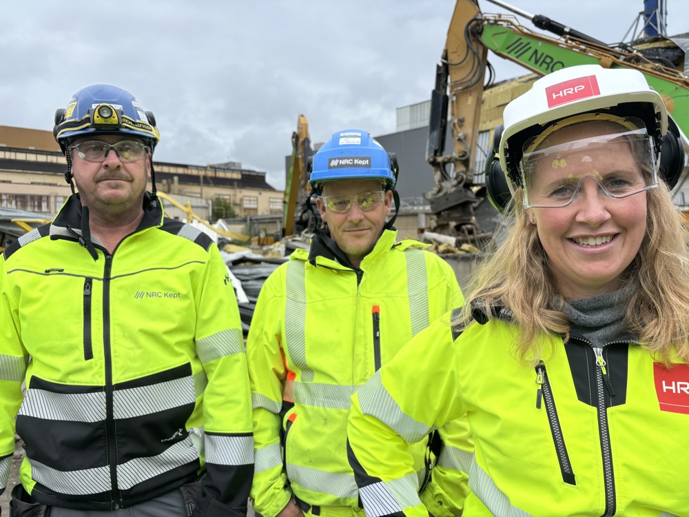 three people, all wearing PPE, posing, standing on a demolition lot.