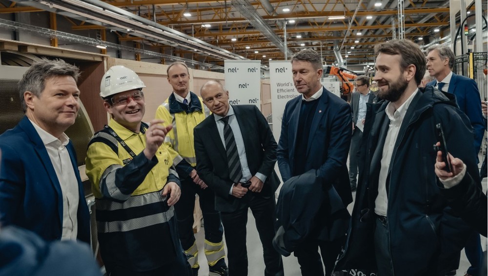 group of visitors in a factory hall, orientation given by man in yellow jacket and white helmet