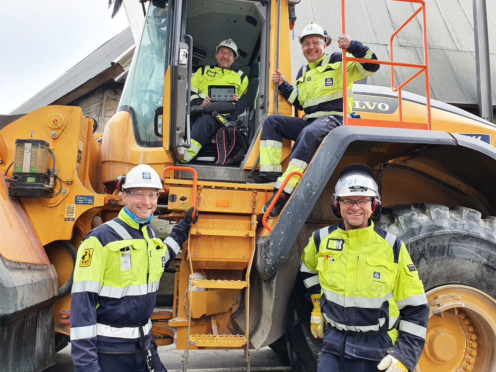 fire menn i arbeidsantrekk står og sitter på stor hjullaster, industri