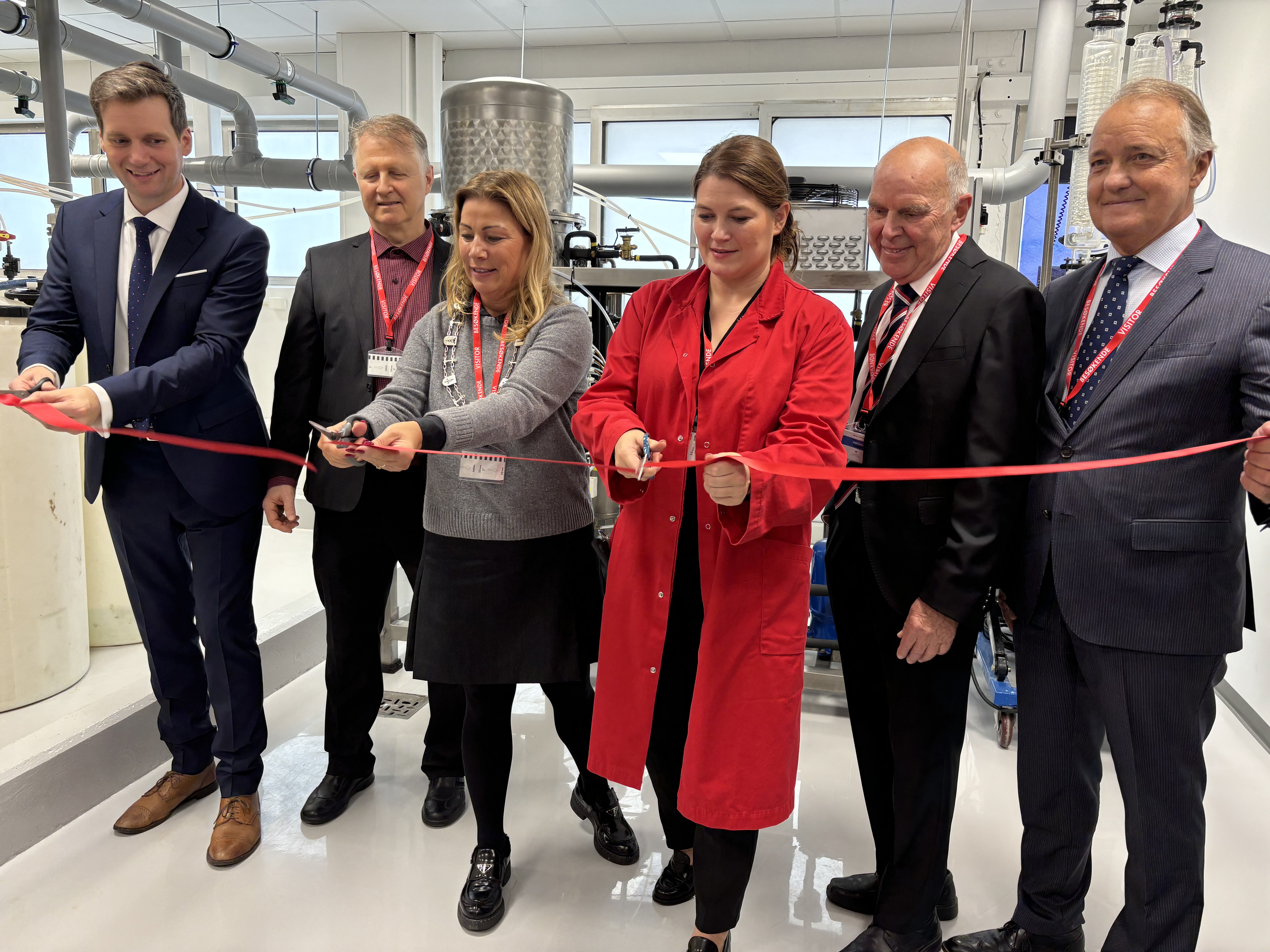 six people standing in a row, holding a red ribbon, three people holding scissors and about to cut the ribbon, opening ceremony of industrial plant