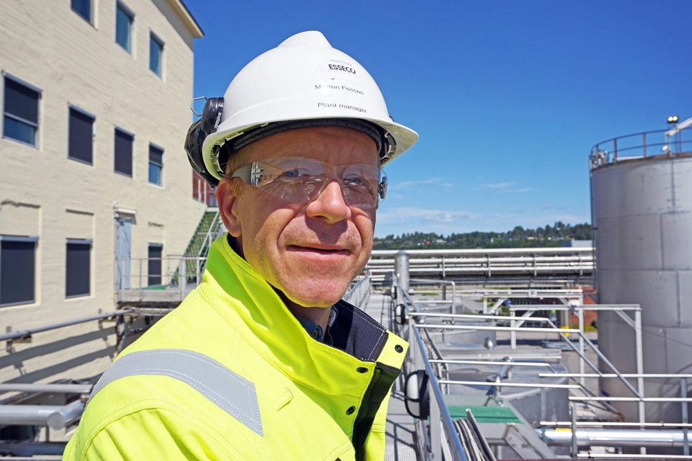 portrait of man, yellow jacket, white helmet, production facilities, blue sky.