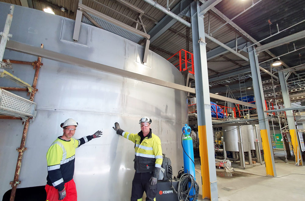 two men leaning on to a big steel tank