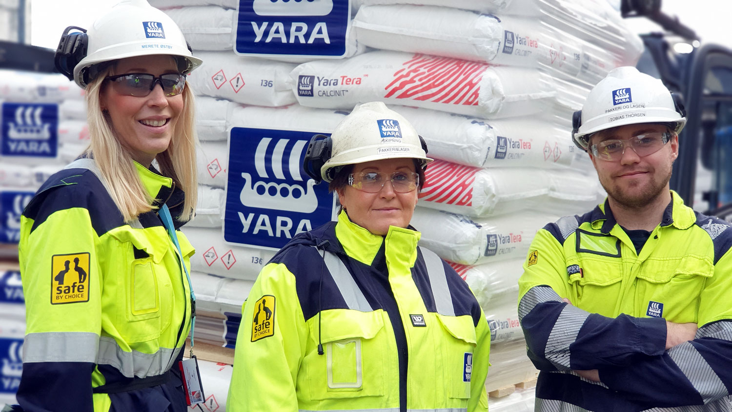 three persons, posing, work clothes, helmets, bags of fertiliser on a pallet