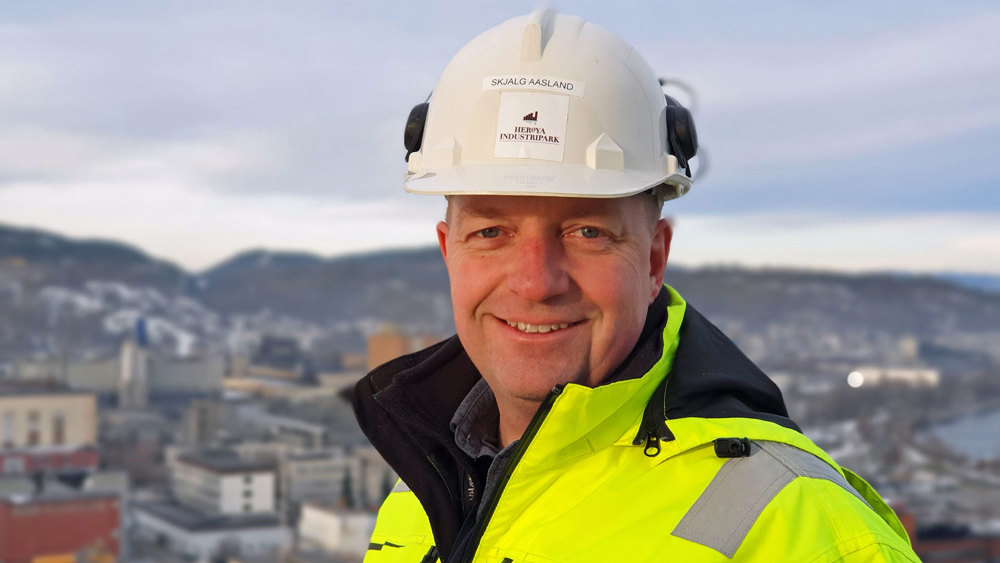 portrait of man, white helmet, yellow jacket, industrial park in background