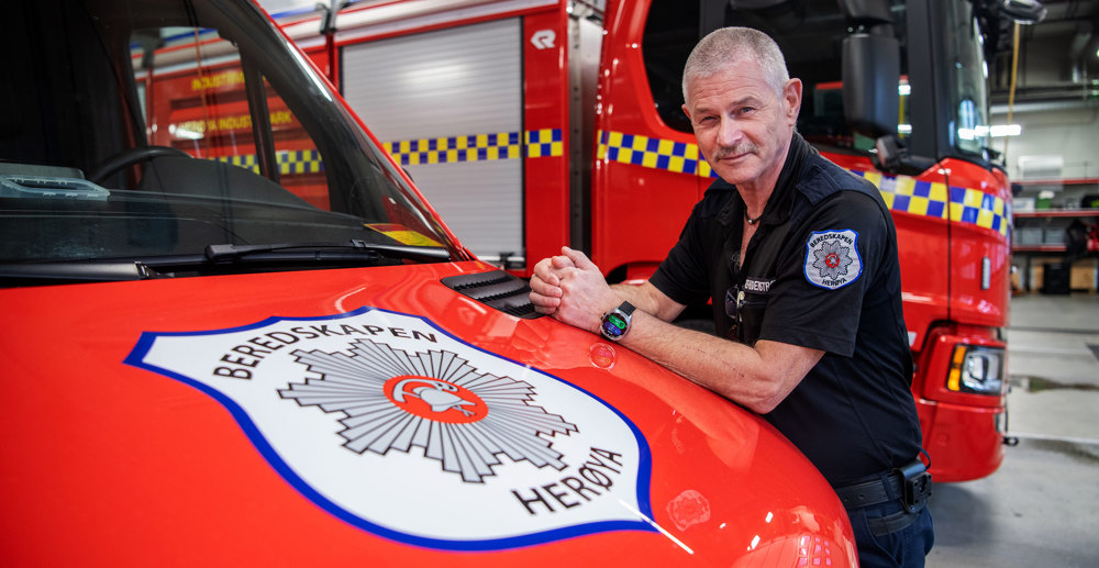 mann, poserer, lener armene mot panseret på et utrykningskjøretøy.