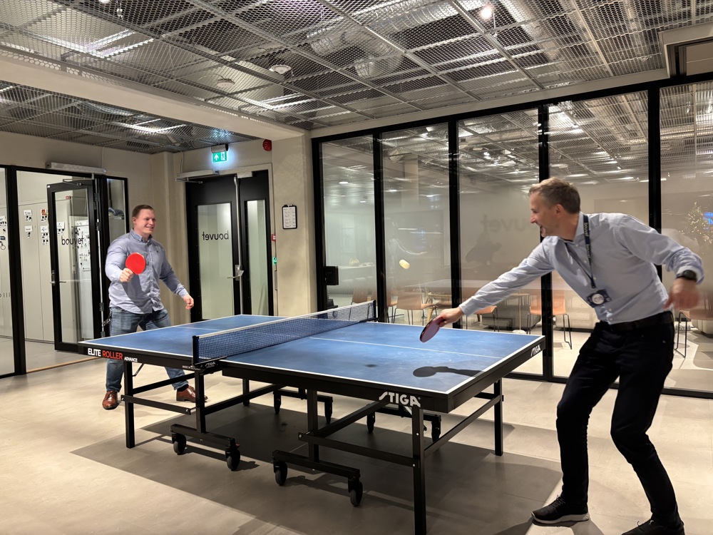 to personer spiller bordtennis, glassvegger, kontormiljø