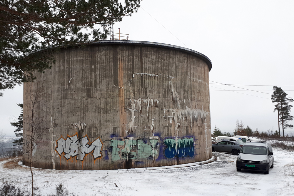 vanntårn, høydebasseng, grå betong, gammel tårn, tagget i bånn, biler parkert på baksiden.