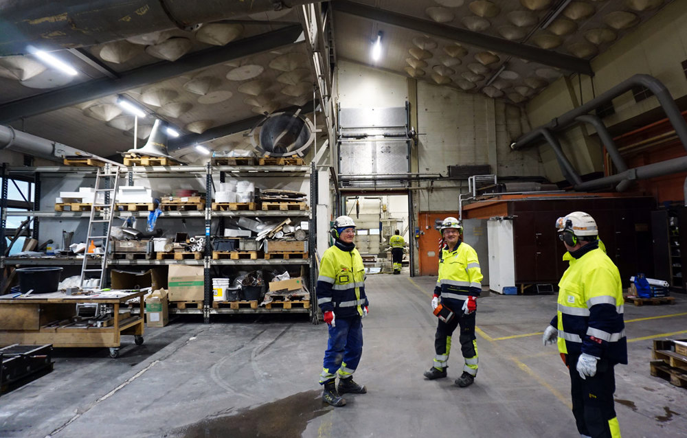 tre menn står i verksted og snakker sammen, arbeidstøy, industri, verneutstyr.