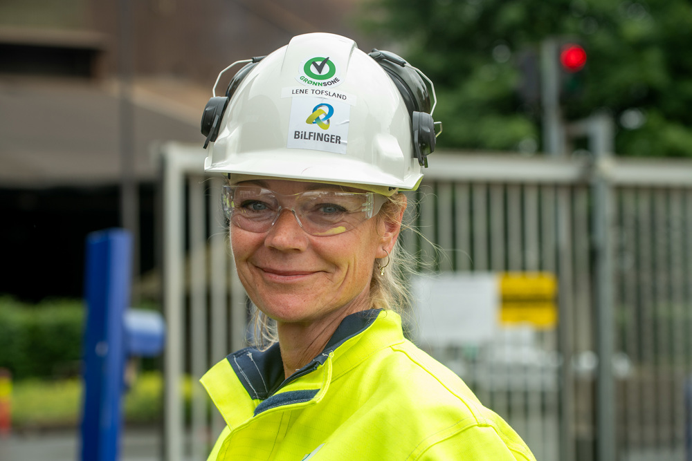portrait of woman, blond hair, goggles, white helmet, yellow and blue helmet, outside factory area.