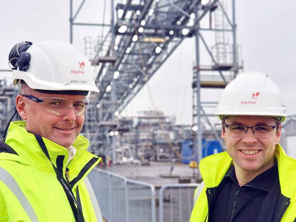 two men, portrait, posing, outside, testing facilities with pipes and fencing in background.