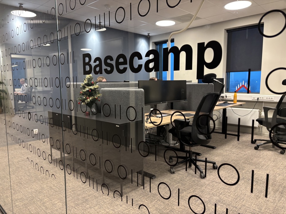 glassvegg med innsikt inn i kontormiljø, navn på avdelingen er trykket på glassveggen.