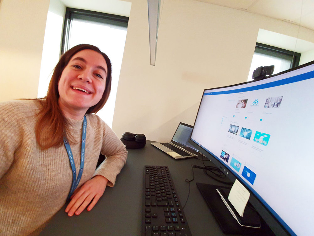 young woman, posing, smiling, sitting by her desk with monitor in front