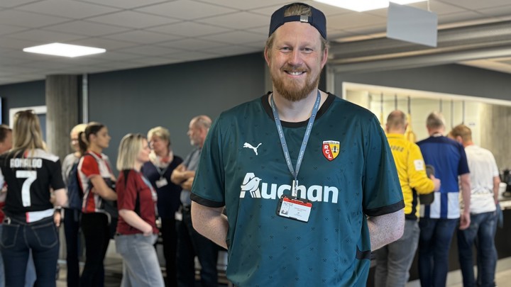 portrett av mann i fotballtrøye og caps, kø med andre personer med fotballtrøye på i bakgrunnen