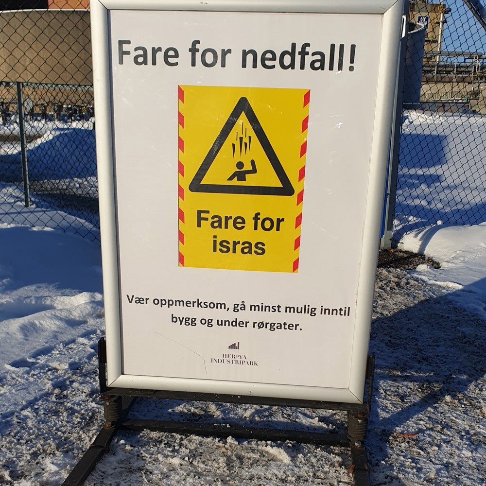 plakat i stativ med melding om fare for nedfall av snø og is fra bygninger og rørbroer