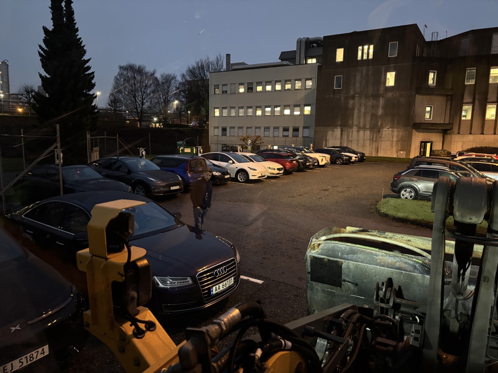 bilparkering. stort kjøretøy og personbiler, en person i mørke klær står ved en personbil.