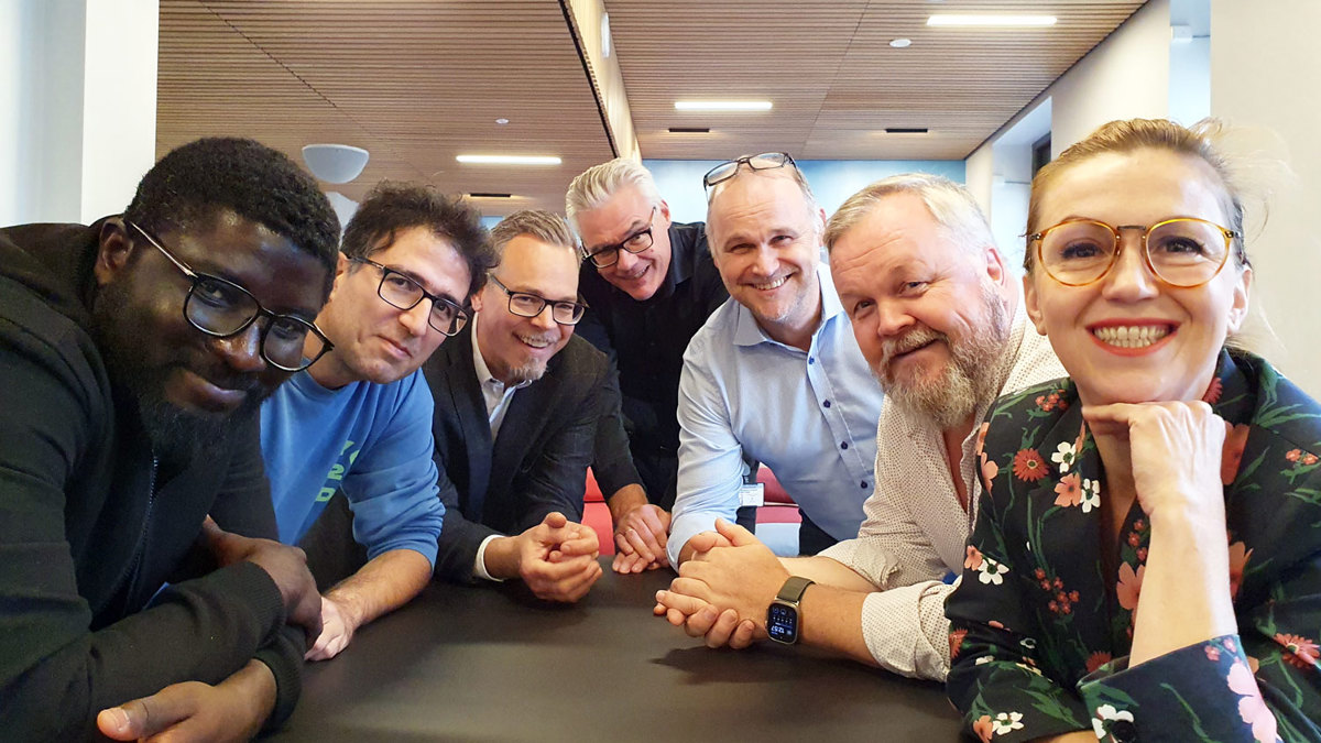 Seven people leaning into the table, standing close together, posing, office environment