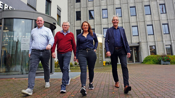 four persons walking towards the camera, posing, office building in the background
